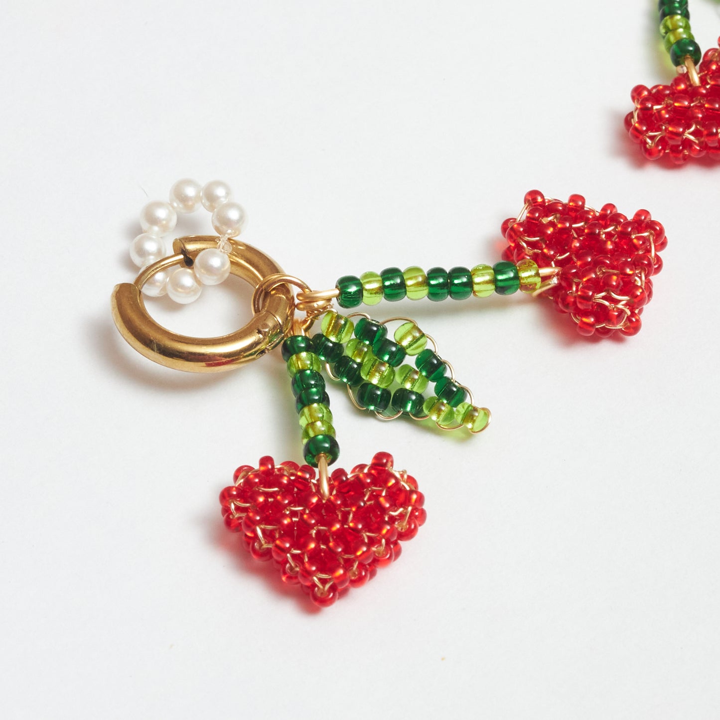 Aretes Berries de Chouette con dije de cerezas en forma de corazón en fondo blanco.