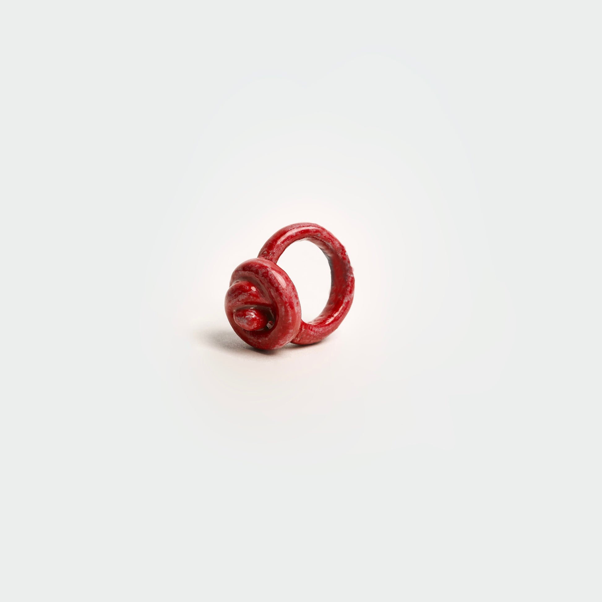 Anillo en fondo blanco hecho a mano en forma  de merengue en materia de cerámica color rojo. 