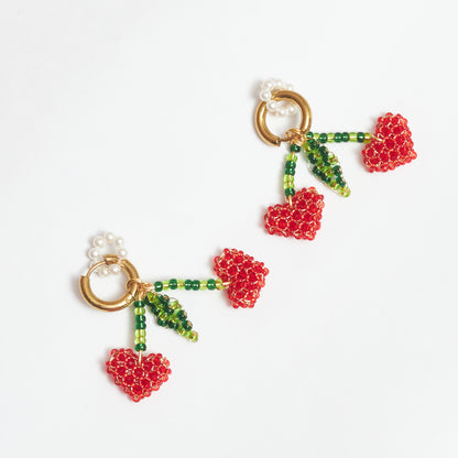 Aretes Berries estilo candonga en acero inoxidable color dorado con dijes en forma de cerezas tejidos artesanalmente con alambre de oro golfi en rocaya de colores verde claro, verde oscuro y rojo y dije circular de perlas.