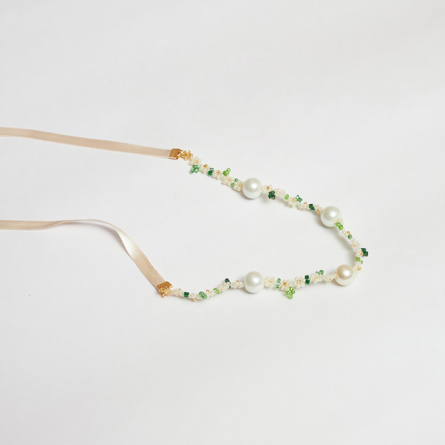 Collar estilo chocker tejido a mano en mostacilla rocaya y múranos brillantes en forma de flores en colores verde claro, verde oscuro, blanco y dorado y cintillas anudadas en forma de moño.
