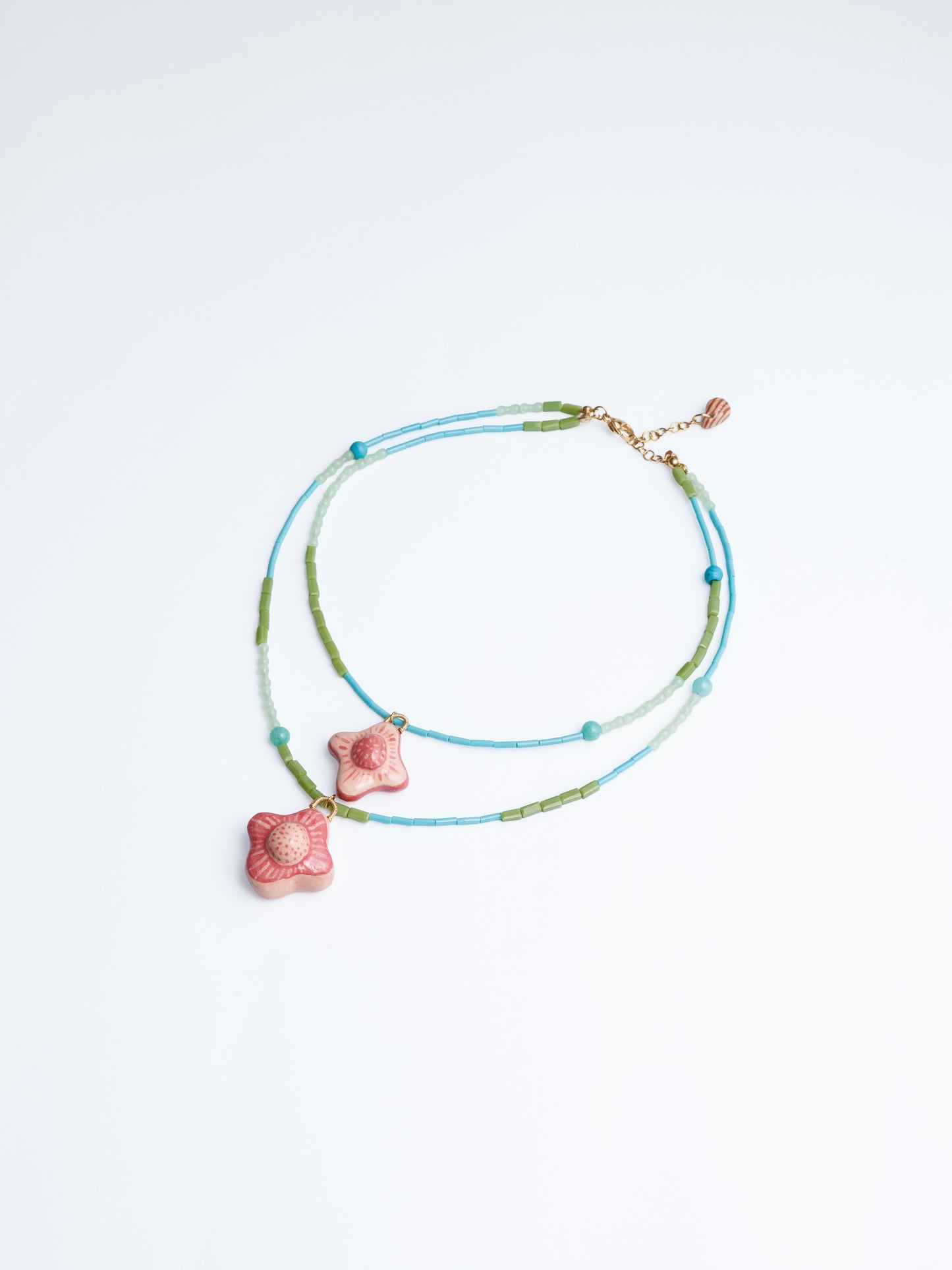 Imagen en fondo blanco de collar doble estilo cascada con doble dije de cerámica con cuencas y cilindros en color azul, turquesa, verde y agua marina de la marca Chouette