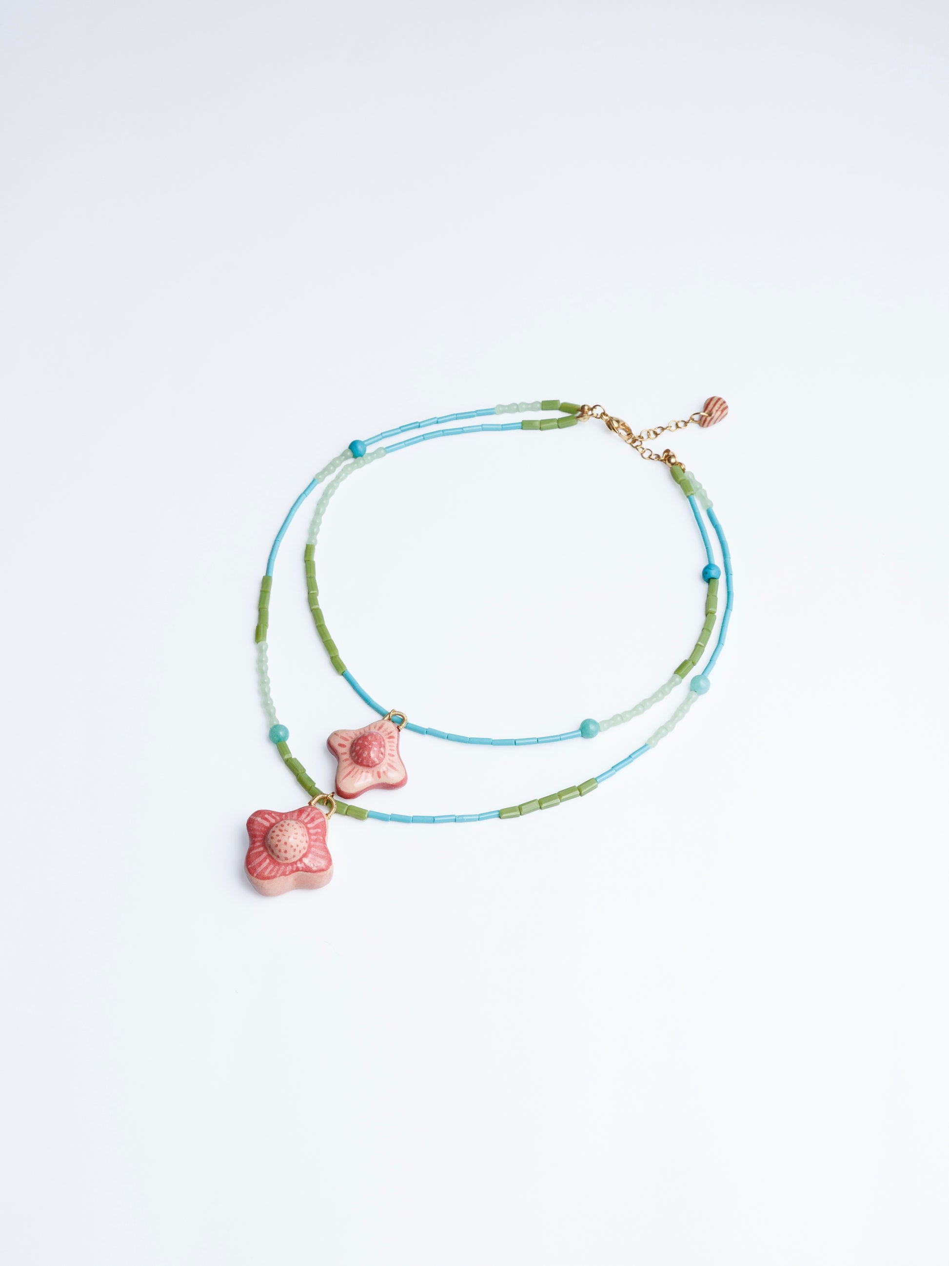Imagen en fondo blanco de collar doble estilo cascada con doble dije de cerámica con cuencas y cilindros en color azul, turquesa, verde y agua marina de la marca Chouette