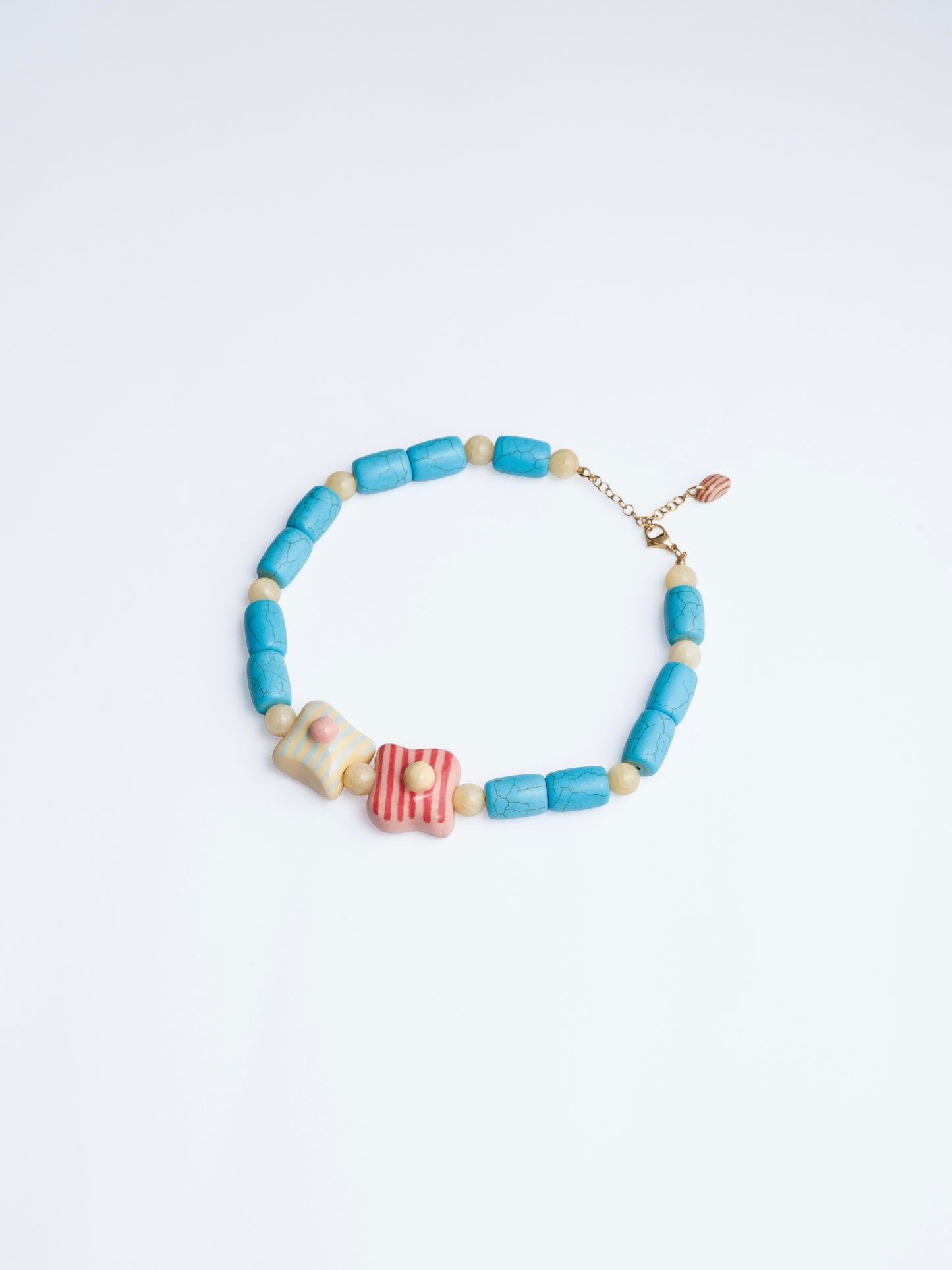 Image en onto blanco del collar de tréboles de chouette con doble dije en colores amarillo, turquesa, rojo y rosa en base de collar de cilindros turquesa y piedra color mantequilla.