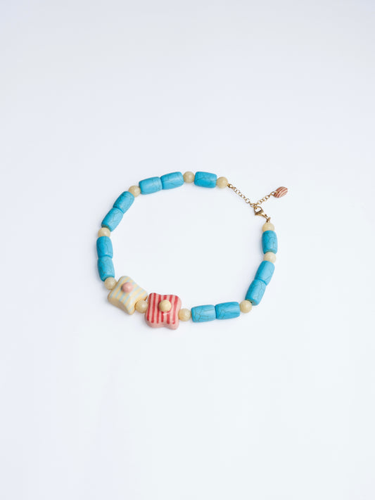 Image en onto blanco del collar de tréboles de chouette con doble dije en colores amarillo, turquesa, rojo y rosa en base de collar de cilindros turquesa y piedra color mantequilla.