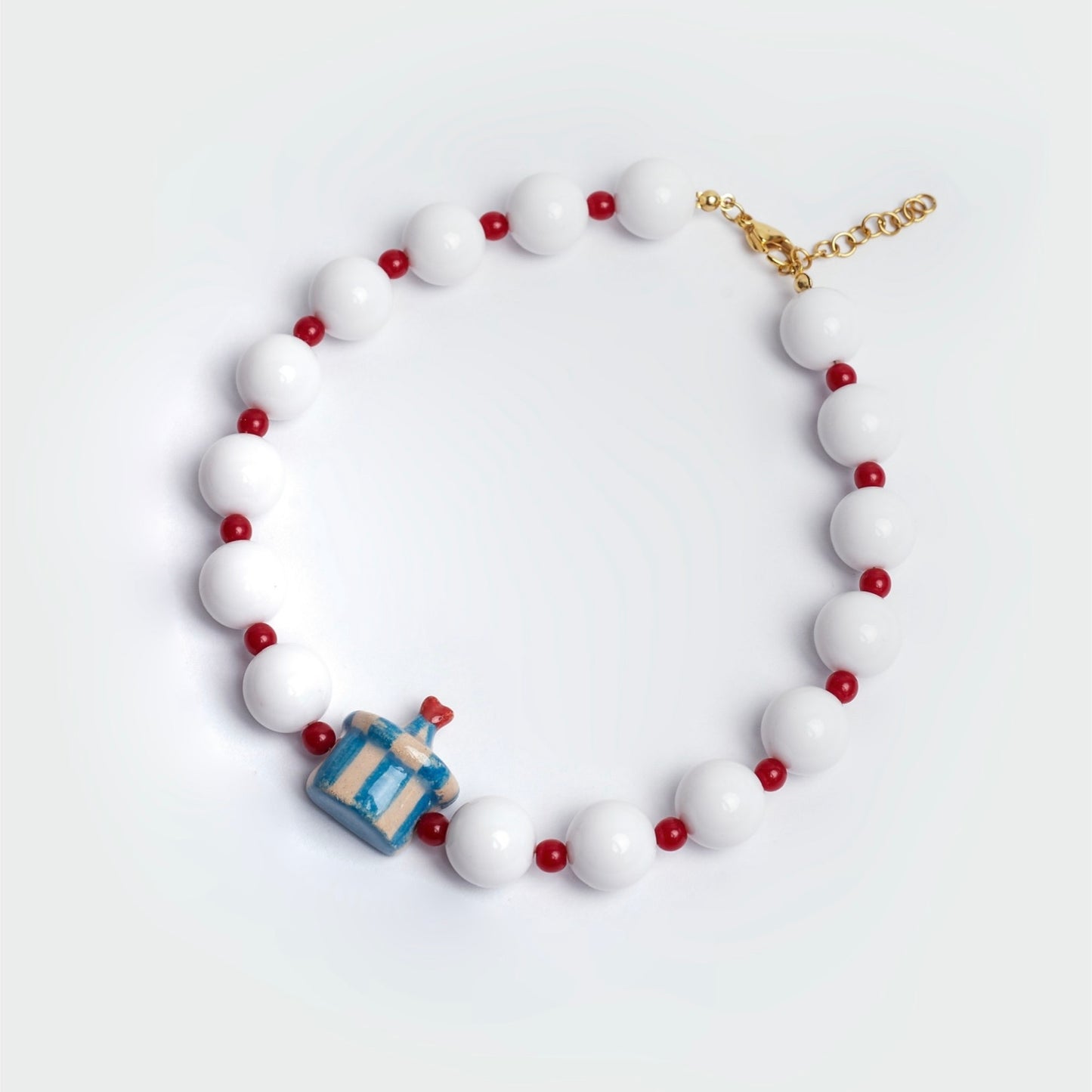 Collar estilo chunky en fondo blanco hecho a mano con perlas blancas y rojas y dije en forma de dulcero a rayas con punta de corazón en colores azul, lanco y rojo.