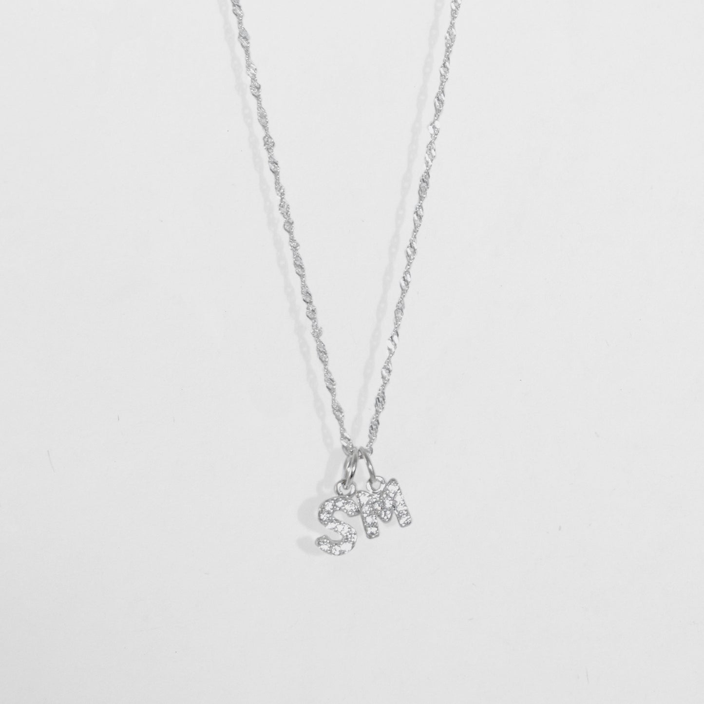 Cadena en material de plata ley 925 en tejido eslabón fino con dije doble con letras S y M con diamantes zircones.