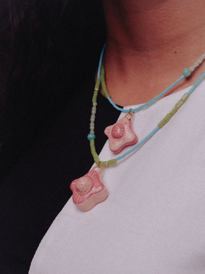 Cuello de modelo de tes morena, utilizando vestido negro con blanco y accesorio estilo cascada con dijes de tréboles en cerámica artesanal con colores rojo y rosa en una base de colla de colores verdes y azules
