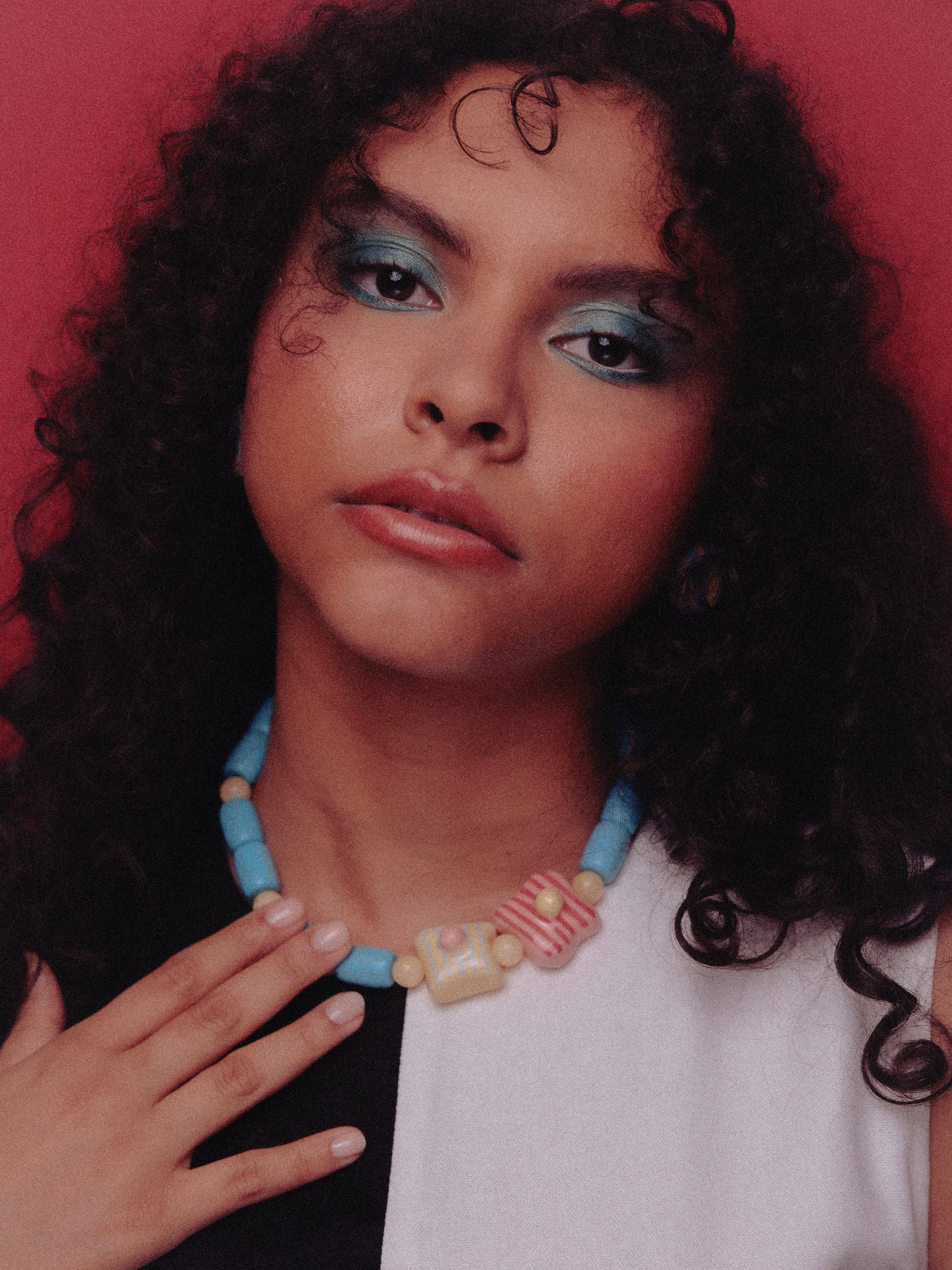 Modelo de tés morena, cabello ondulado y ojos negros, usando collar de tréboles heirloom y vestido blanco y negro.