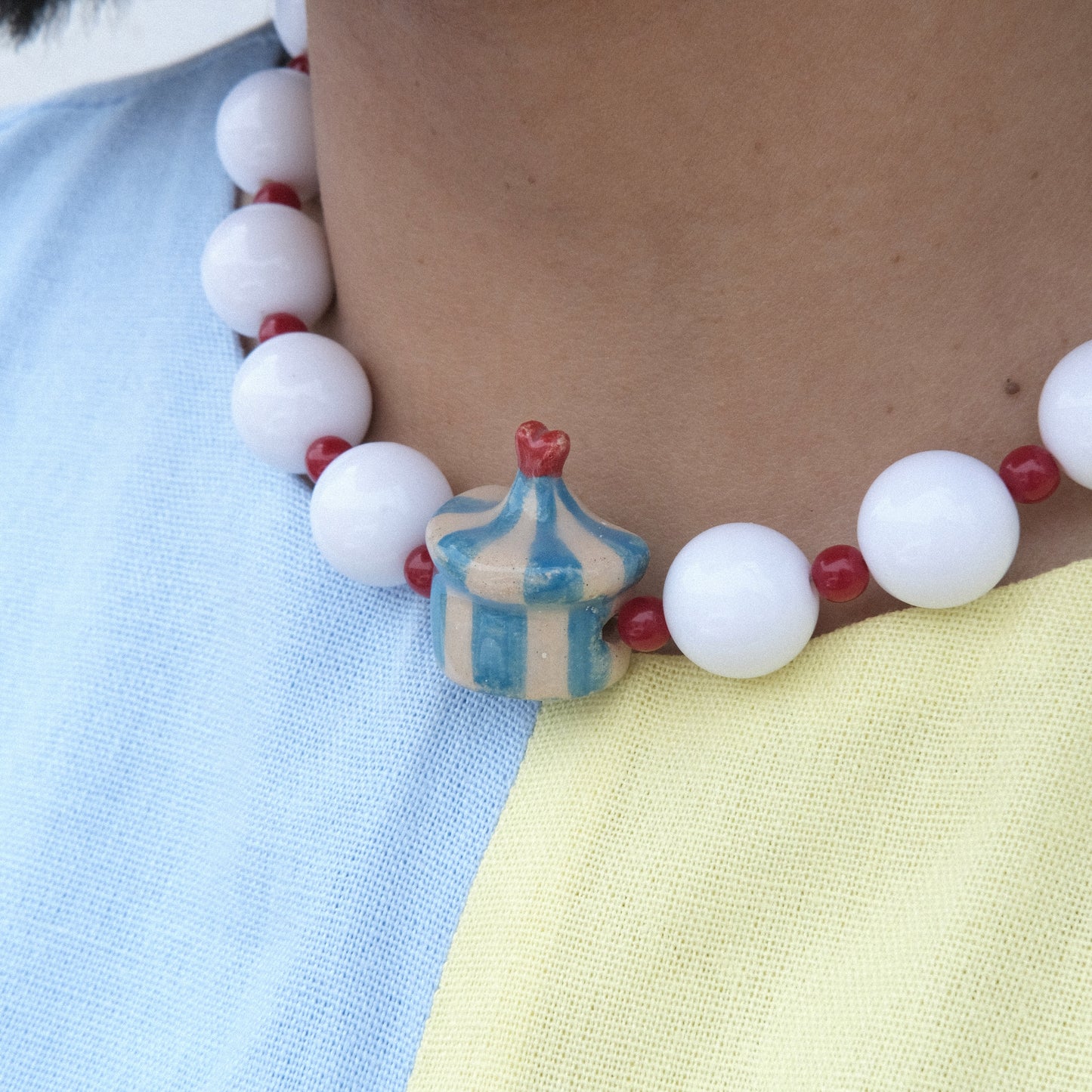 Cuello de modelo de tes morena usando un vestido celeste y amarillo y collar Dulcero Festival Mora Azul.