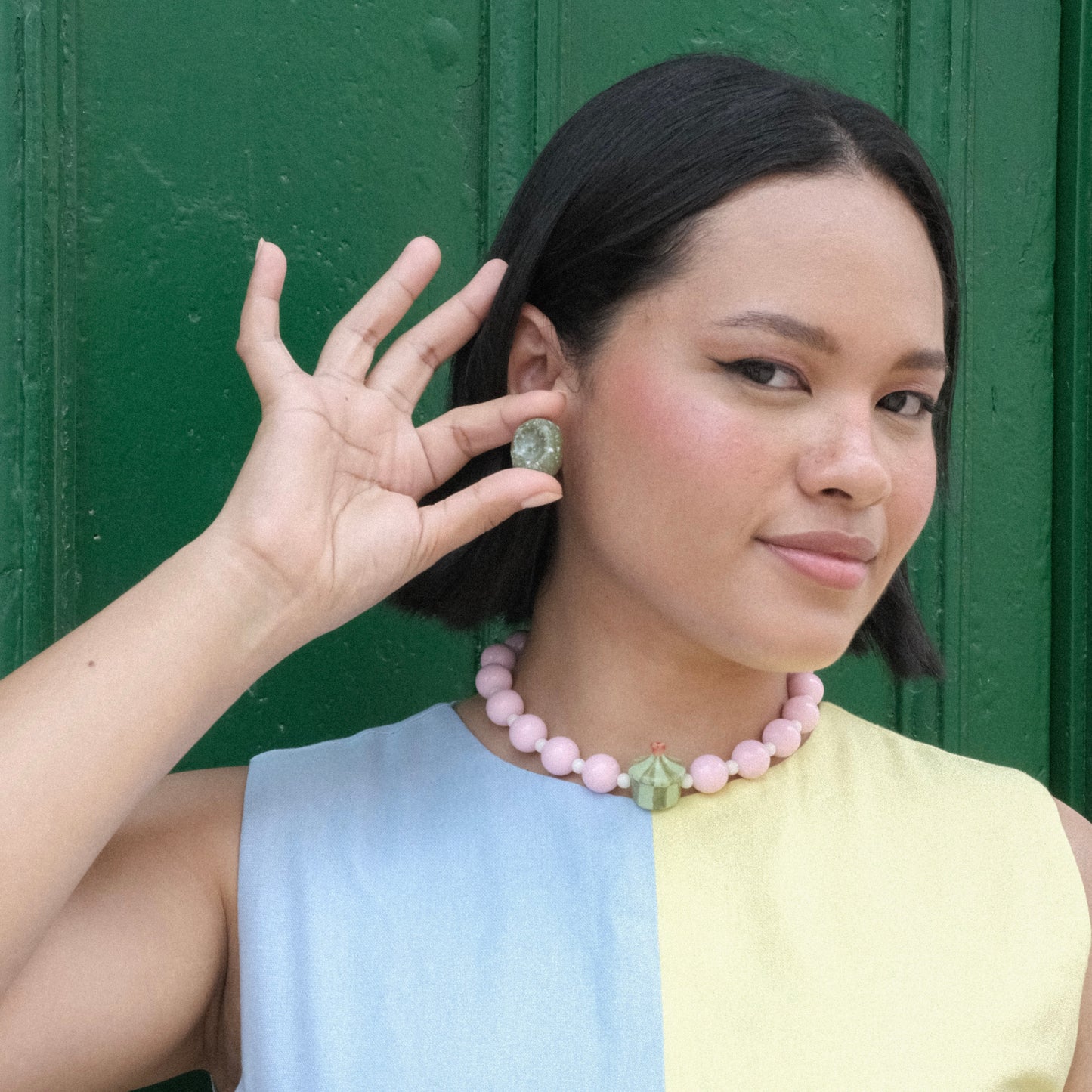 Modelo pluszize de tes morena y cabello corto en color negro usando aretes Deliciosos Apio, colla dulcero de cidra en material de cerámica y en colores verde claro y oscuro y vestido amarillo y azul.