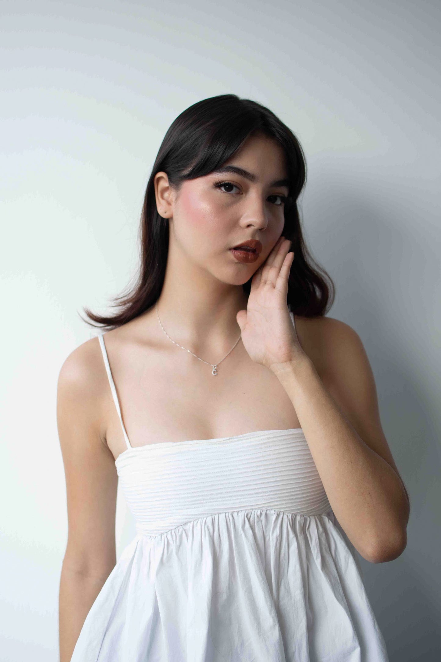 Modelo de tes blanca y cabello negro, usando un vestido blanco y cadena de plata con dije de letra personalizable.