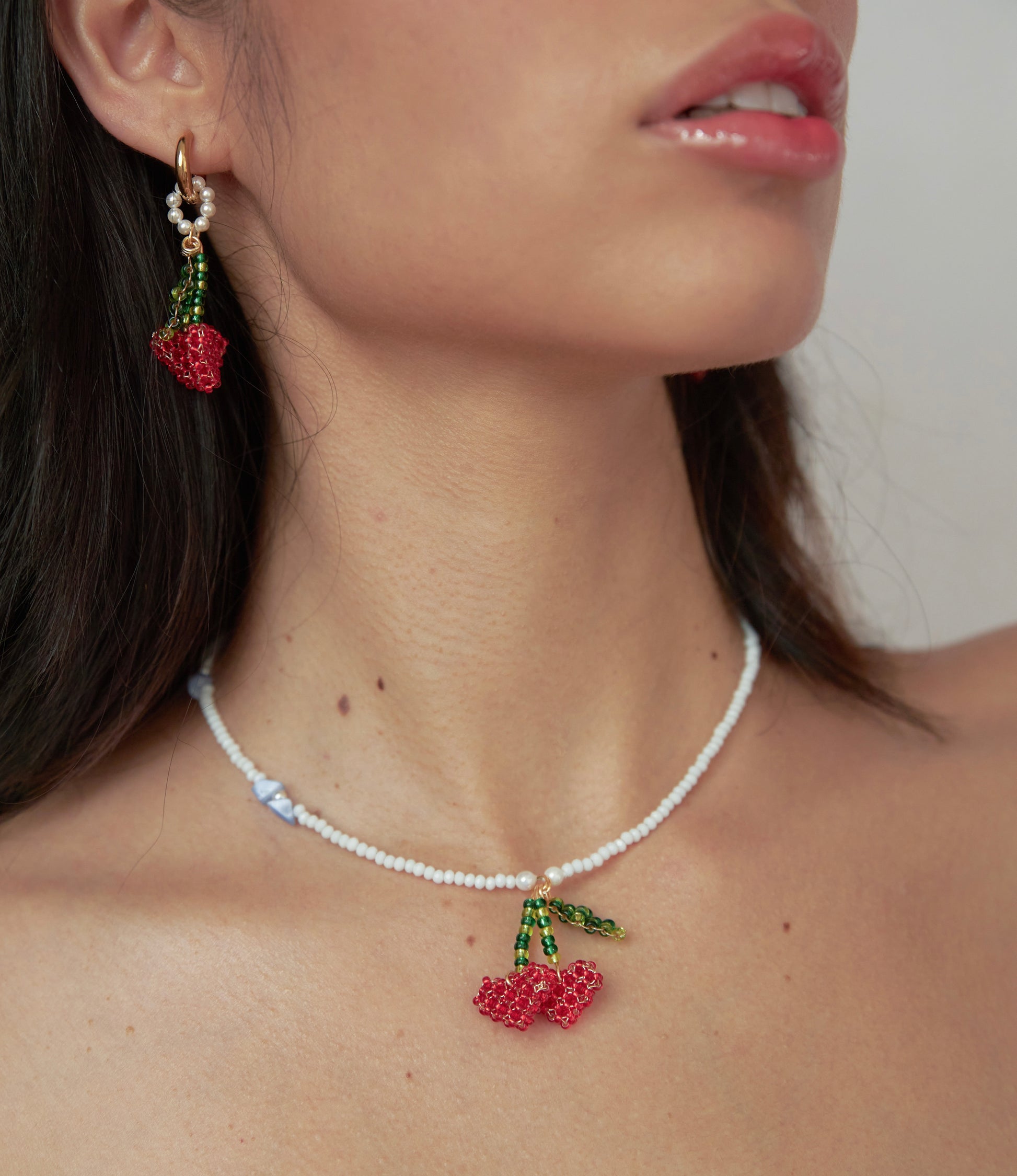 Cuello de modelo de tes blanca y cabello negro usando set Berries de Chouette que incluye candongas y collar de cerezas en forma de corazón tejidas a mano