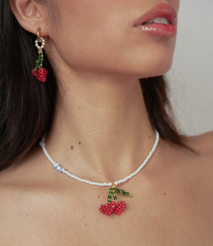 Cuello de modelo de tes blanca y cabello negro usando set Berries de Chouette que incluye candongas y collar de cerezas en forma de corazón tejidas a mano