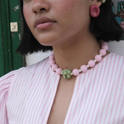 Rostro y cuello de modelo pluszize de tes morena   cabello corto color negro, usando top de rayas en colores blanco y rosado, Collar Dulcero Cidra estilo chunky y aretes deliciosos en colores rojo, verde claro y verde oscuro en material de cerámica. 