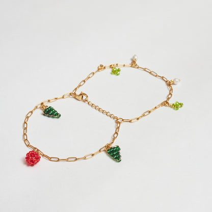 brazalete de doble cadena abierto en estilo mariposa, en material de acero inoxidable color dorado con dijes de perlas blancas y en mostacilla tejida  con forma de árbol, flor y fruto rojo en colores verde claro, verde oscuro y rojo. 
